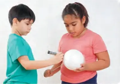 Fotografía de Agustín y Alejandra: él sostiene un plumón y ella una pelota blanca de plumavit, representando la Tierra con una marca.