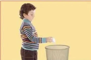 Niño botando un papel arrugado en un basurero.