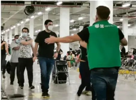 Fotografía de personas con mascarillas en un centro de vacunación, indicando distanciamiento y organización.