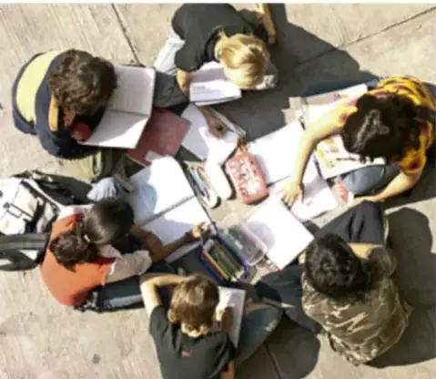 Fotografía cenital de un grupo de estudiantes sentados en círculo sobre el suelo, trabajando con cuadernos y materiales escolares; crédito a Carlos Loza / CONALITEG.