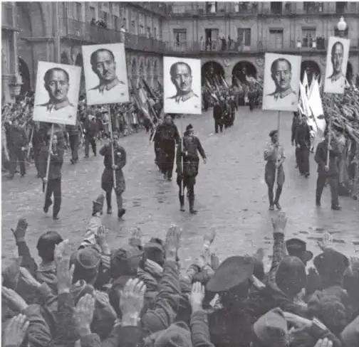 Fotografía histórica en blanco y negro de una marcha o desfile con retratos enmarcados de figuras (posiblemente políticas) portados por participantes, con público saludando, en una plaza urbana con arquitectura clásica, referente del periodo de entreguerras o del ascenso del fascismo.