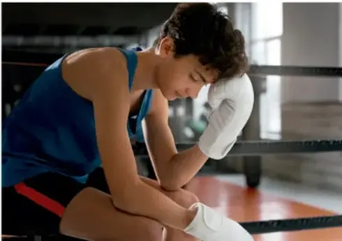 Joven atleta con vendaje en la mano descansando sentado en un ring de boxeo.