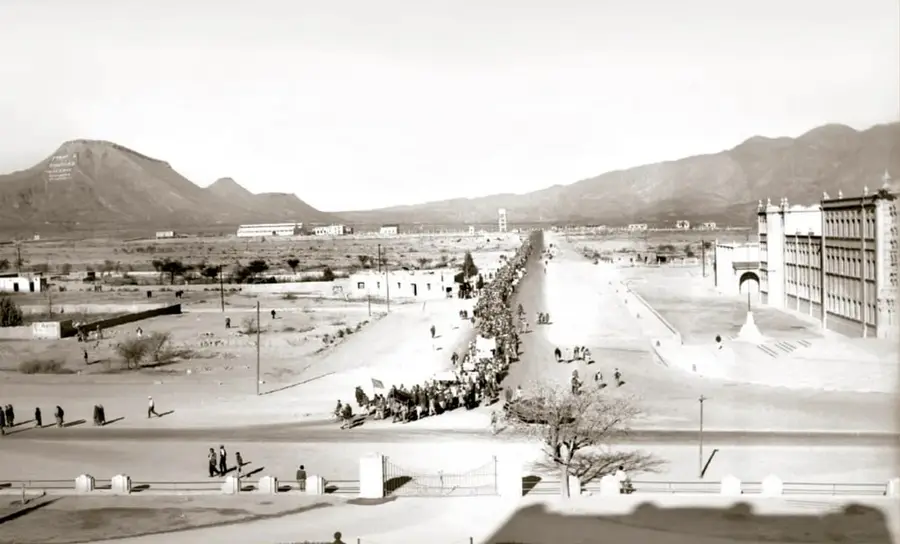 Fotografía histórica en sepia de la Caravana del hambre de Nueva Rosita, 1951: larga columna de mineros marchando por la avenida central de la ciudad, con montañas al fondo y edificios a los costados. Crédito: SECRETARÍA DE CULTURA. INAH. SINAFO.FN.MX.