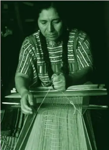 Fotografía a color (en tonos verdes en la reproducción del libro) de una mujer triqui tejiendo en un telar de cintura, con huipil bordado, pelo largo en dos trenzas, sosteniendo el hilo que pasa por la trama.