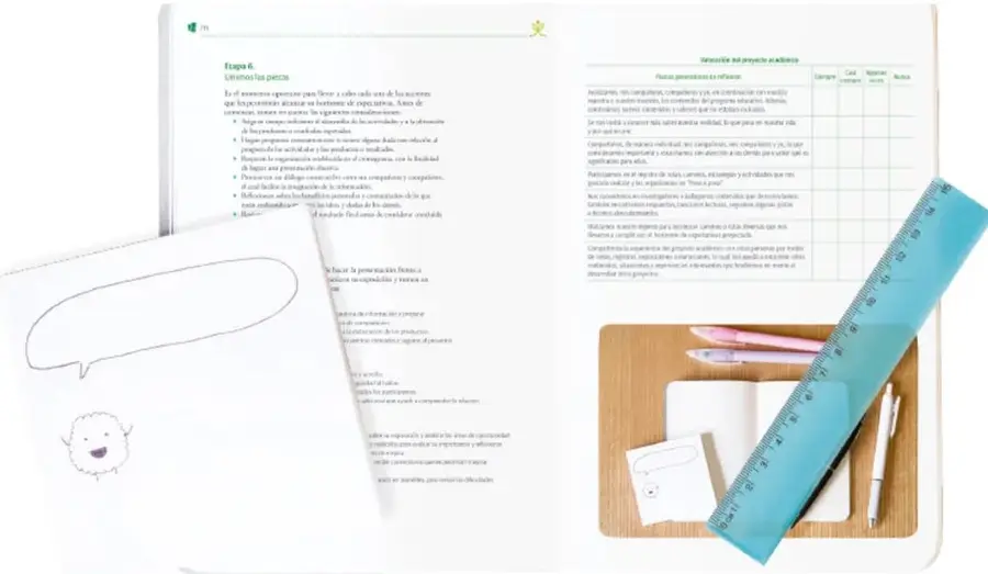 Fotografía de una mesa de estudio con una regla azul transparente, lápices, tarjetas de notas, un cuaderno pequeño y un portapapeles de madera, que ilustran el registro y la planeación del proyecto académico.