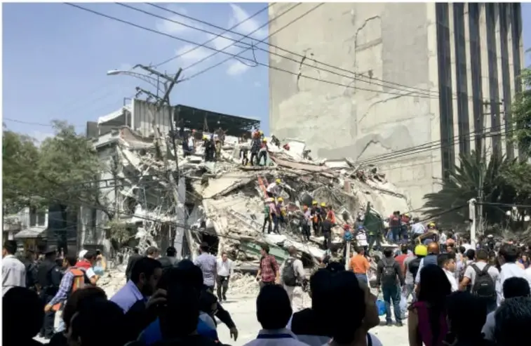 Fotografía documental de un edificio derrumbado rodeado de escombros, con brigadas de voluntarios y un gran número de ciudadanos participando en labores de rescate tras el sismo de 2017.