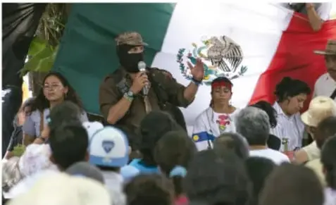 Comandante del EZLN hablando ante una multitud con bandera de México.