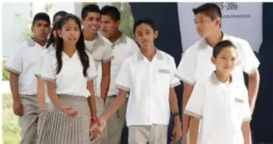 Grupo de estudiantes de secundaria uniformados posando frente a un edificio escolar.