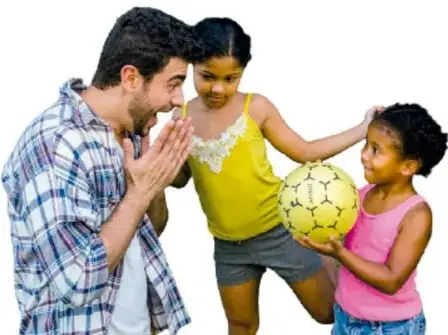 Tres personas (un hombre adulto, una niña y un niño) juegan con un balón de fútbol; la niña sostiene el balón.