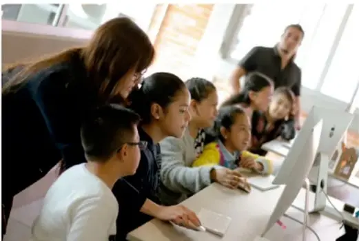 Estudiantes y docente frente a una computadora, trabajando en equipo.