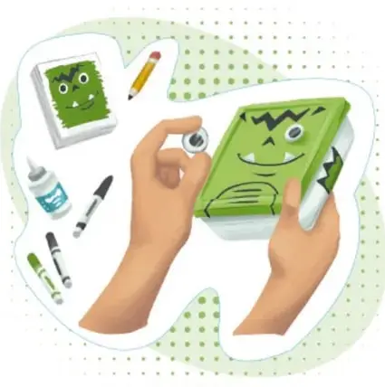 Manos sosteniendo el recipiente verde decorado como personaje, con plumones, pegamento y lápiz alrededor.