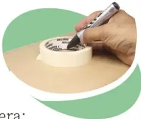 Mano trazando un círculo con plumón sobre una caja, apoyando un rollo de cinta como guía.