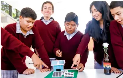 Fotografía de cinco estudiantes de telesecundaria con uniforme rojo trabajando alrededor de una mesa con materiales escolares: calculadora, fichas y un frasco con un experimento.