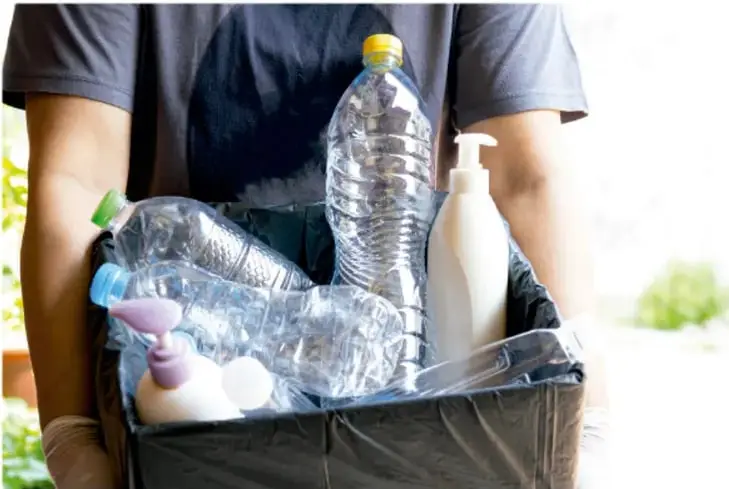 Fotografía de una persona sosteniendo un bote de basura con botellas de plástico y envases, que ilustra el manejo de residuos.