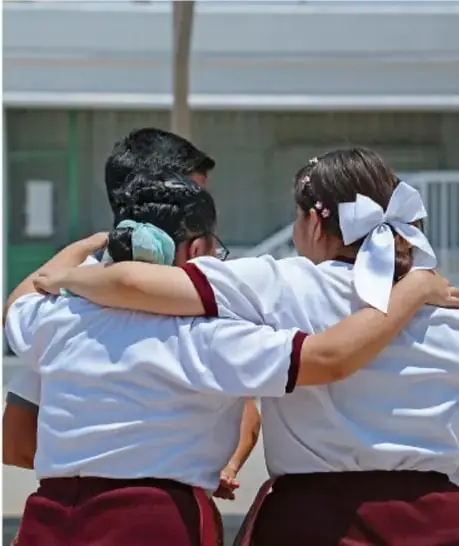 Fotografía de tres estudiantes de telesecundaria de espaldas, con los brazos entrelazados sobre los hombros, símbolo de compañerismo e inclusión.