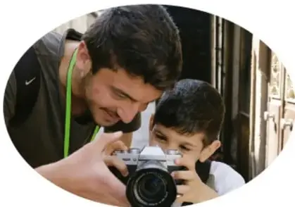 Persona adulta enseñando a un niño a usar una cámara fotográfica.