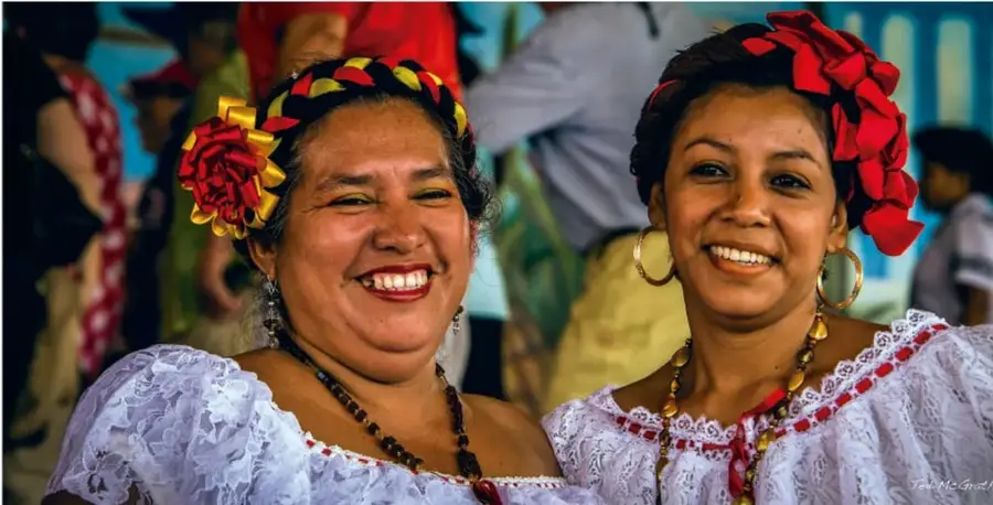 Fotografía de dos mujeres sonrientes con vestimenta tradicional veracruzana (blancas de encaje con bordado rojo, flores rojas y listones amarillos y rojos en el cabello, aretes y collares), en aparente fiesta o celebración popular.