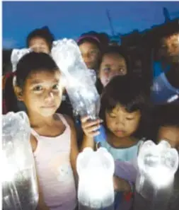 Niños al atardecer sosteniendo botellas con agua encendidas por la luz.