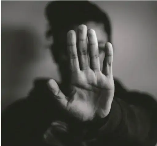 Fotografía en blanco y negro de una persona levantando la mano en gesto de "alto" o detención, sugiriendo rechazo a la violencia.