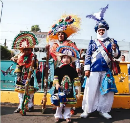 Foto de personas con trajes típicos coloridos y plumas, posiblemente de una tradición o danza regional mexicana.