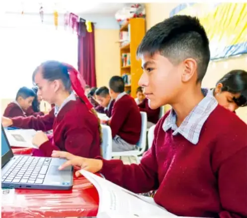 Estudiantes de telesecundaria trabajando con computadoras y libros en el aula.