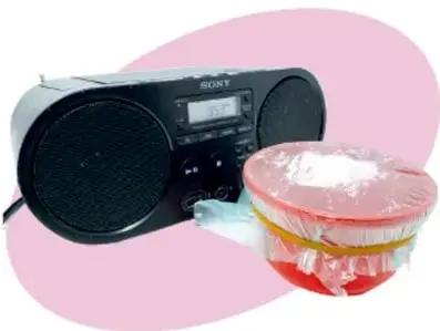 Radio o grabadora negra con un recipiente transparente cubierto con plástico y arena encima.