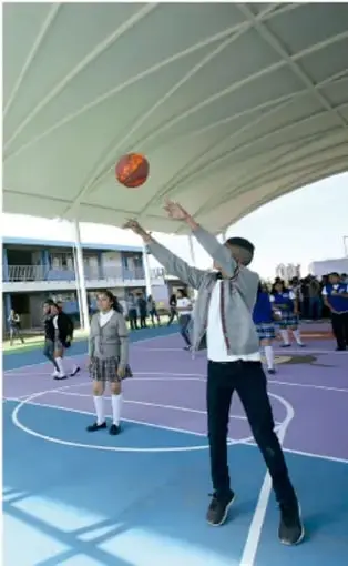 Fotografía de estudiantes en una cancha de basquetbol techada, uno de ellos lanzando el balón.