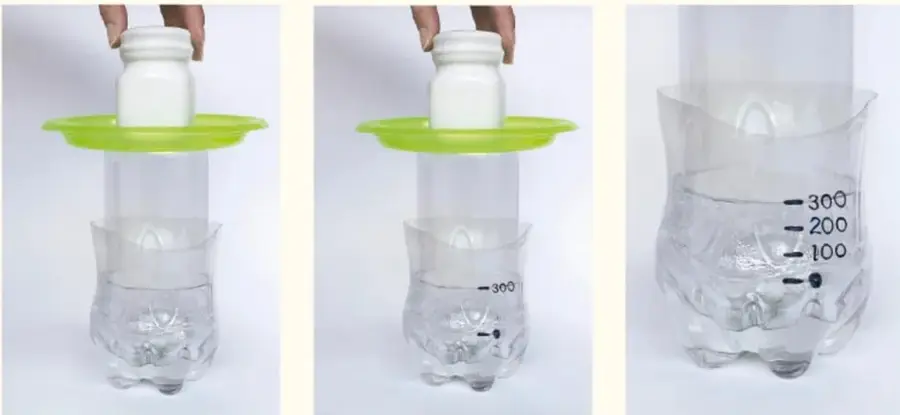 Mano colocando una botella pequeña sobre la tapa verde de la balanza; el recipiente contiene agua.