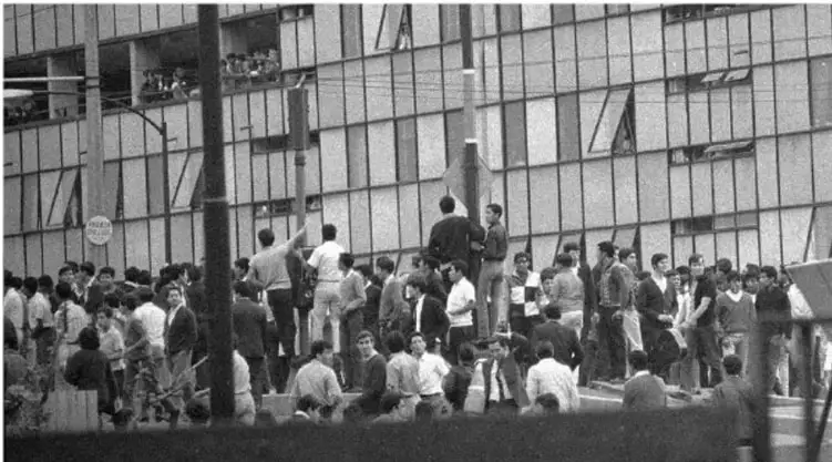 Fotografía en blanco y negro de una multitud de estudiantes reunidos frente a un edificio de varios pisos, posiblemente durante una protesta o asamblea.