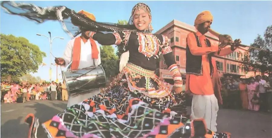 Presentación cultural en la India con una bailarina vestida con un traje tradicional y músicos que tocan instrumentos de percusión frente a una multitud.