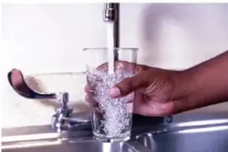 Manos llenando un vaso con agua de una llave, representando el consumo de agua simple.