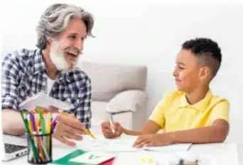 Fotografía de un adulto mayor y un niño sentados en una mesa, conversando y tomando notas; representa la entrevista comunitaria.