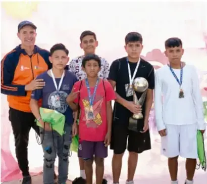 Fotografía de un grupo de jóvenes con medallas y trofeo junto a un adulto, probablemente tras una actividad o logro deportivo/comunitario.
