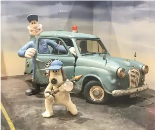 Fotografía de figuras de plastilina: un cartero de uniforme junto a una camioneta verde y un perro con gorra al frente, típica escena de animación en stop motion.