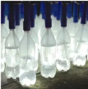 Fila de muchas botellas de plástico con agua colocadas en un techo, brillando con la luz del sol.