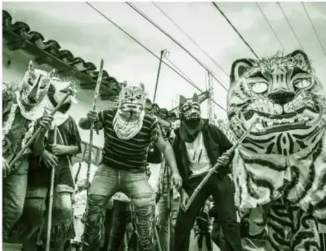 Fotografía de varios peleadores con máscaras pintadas de jaguar o tigre, algunos con látigos, durante la pelea de tigres de Zitlala.