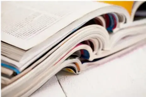Fotografía de varias revistas o libros abiertos apilados con hojas de colores, mostrando su interior.
