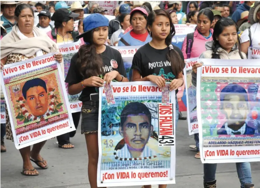 Fotografía de una marcha: mujeres y jóvenes portan carteles con el rostro de los estudiantes desaparecidos de Ayotzinapa con las consignas «¡Vivo se lo llevaron!», «¡Con VIDA lo queremos!», «¡Ayotzinapa vive!» y «¡Los fululanes 43!».