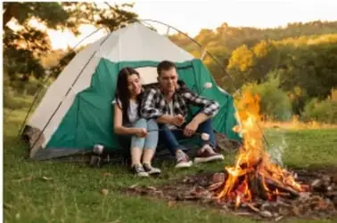 Fotografía de una fogata junto a una casa de campaña, con dos personas sentadas; ilustra la combustión como proceso exotérmico.