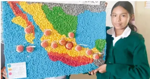 Fotografía de una estudiante de telesecundaria en uniforme verde sosteniendo una maqueta o mapa tridimensional de México elaborado con materiales reciclados (tapas de botella) que muestra regiones de colores con algunas etiquetas rojas.