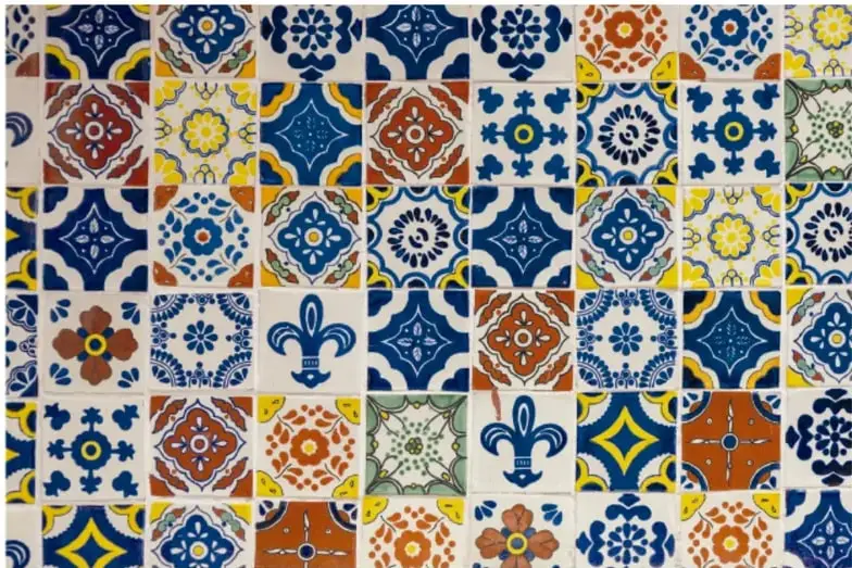 Mosaico rectangular de azulejos de talavera con diseños geométricos y florales en colores azul, blanco, naranja y amarillo, formando un patrón repetitivo.