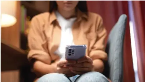 Persona sentada usando un teléfono celular en un ambiente interior.