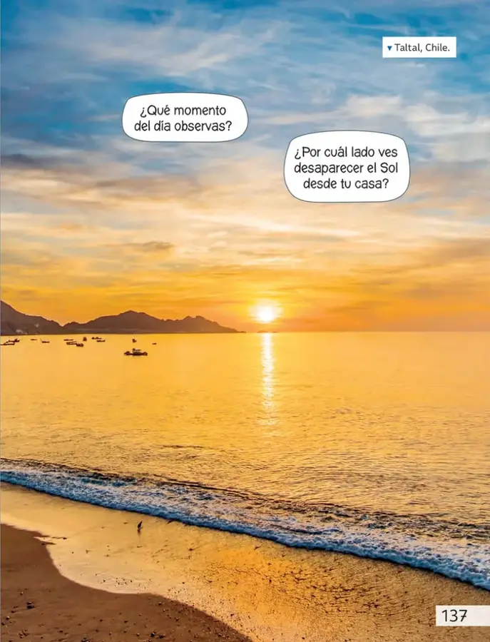 Fotografía de una playa al atardecer en Taltal, Chile: el Sol se oculta tras el horizonte del mar, el cielo y el agua se tiñen de naranja y hay botes y cerros al fondo.