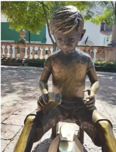 Estatua de bronce del niño bolero: niño sentado en su banquillo lustrando un zapato.