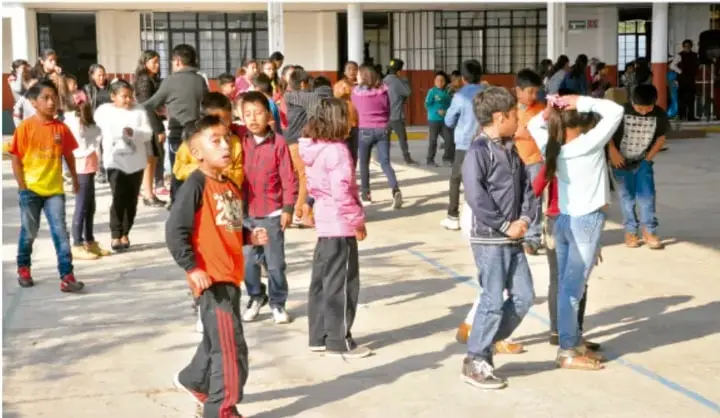 Fotografía de estudiantes de primaria en el patio de una escuela, conversando y caminando en grupo durante el recreo.