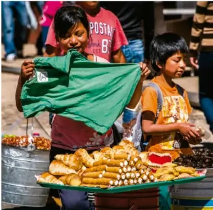 Fotografía de dos niños vendiendo pan y frutas en un puesto callejero, uno de ellos sostiene una prenda verde. Ilustra el trabajo infantil y la desigualdad socioeconómica.