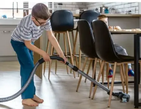 Niño aspirando el piso de una cocina, realizando una tarea del hogar.