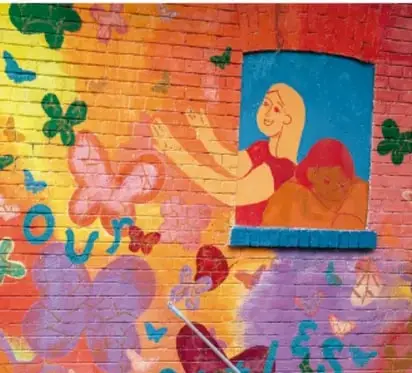 Mural colorido pintado en una pared de ladrillo, con figuras de personas, mariposas y hojas, relacionado con una exposición artística escolar.