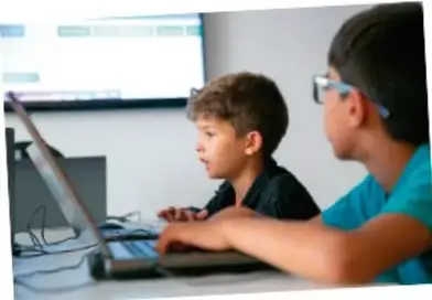 Dos niños frente a una computadora consultando información en internet.