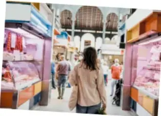 Fotografía de un pasillo de un mercado con puestos de productos en vitrinas y una persona caminando de espaldas.